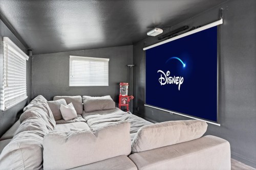 Cozy living room with a large gray sectional sofa and a Disney movie screen on the wall. Bright, modern decor.