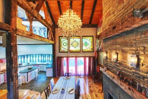 A spacious, rustic dining area with a chandelier, stained glass windows, and wooden beams, featuring a long table.