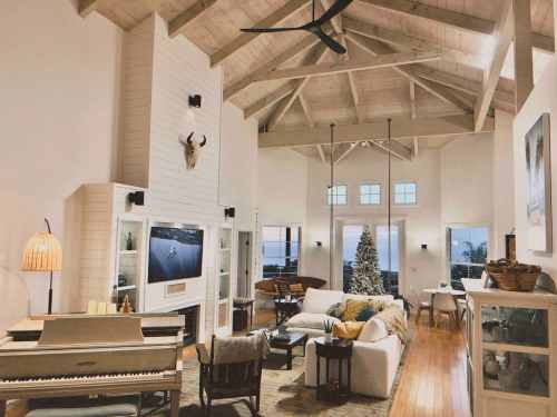 Bright, airy living room with high ceilings, a piano, cozy seating, and a view of the ocean through large windows.