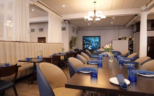 A modern restaurant interior with blue accents, featuring tables set with blue glasses and a cozy atmosphere.