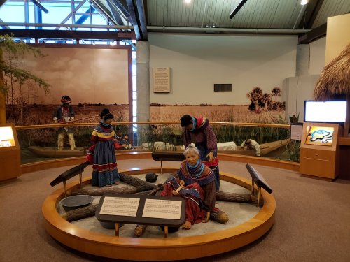 A museum exhibit featuring life-sized figures of Indigenous people in traditional clothing, set in a natural landscape.