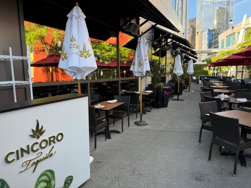 Outdoor dining area of Cincoro Tequila with tables, umbrellas, and a view of city buildings in the background.