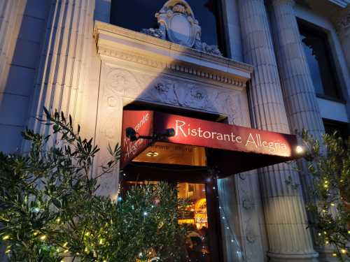 Entrance of Ristorante Allegria, featuring ornate architecture and greenery, illuminated at dusk.