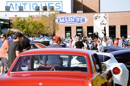 A bustling outdoor event with crowds near antique shops and classic cars on display under a clear sky.