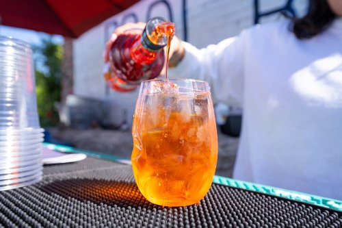 A close-up of a glass filled with an orange drink being poured from a bottle, set on a bar counter.