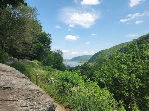 A scenic view of a river valley surrounded by lush green hills and a clear blue sky with scattered clouds.
