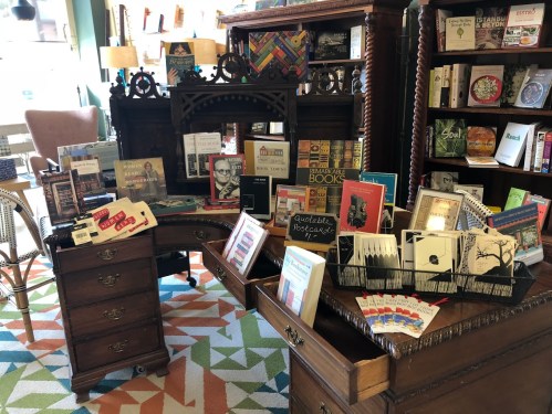 A cozy bookstore display featuring books, postcards, and decorative items on a vintage wooden table and shelves.