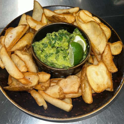 A plate of crispy potato wedges surrounding a bowl of guacamole with lime wedges.
