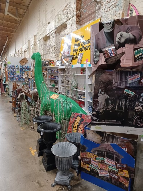A vintage store aisle filled with eclectic items, including a green dinosaur, old signs, and various decorative objects.