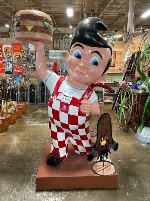 A large, cheerful statue of a boy in checkered overalls holding a burger, surrounded by various decorative items.