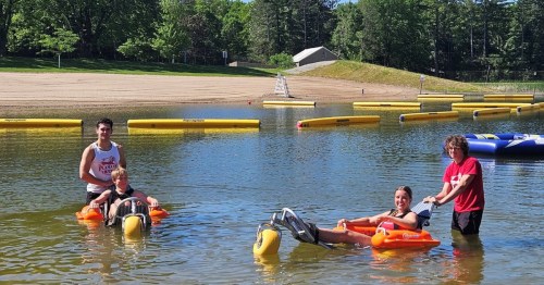 People using adaptive floating wheelchairs in a lake at Plamann Park, WI.