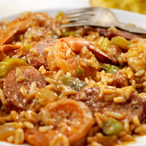 A close-up of a plate of shrimp and sausage jambalaya with rice and vegetables, garnished with a fork.