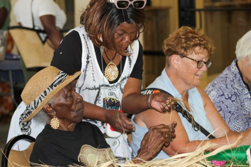 A group of women engaged in a crafting activity, with one assisting an elderly woman in weaving.