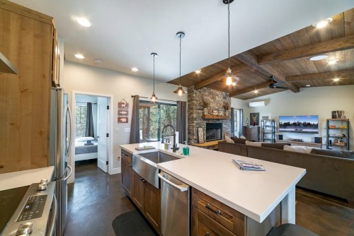 Modern kitchen with wooden cabinets, a large island, and a living area featuring a stone fireplace and cozy seating.