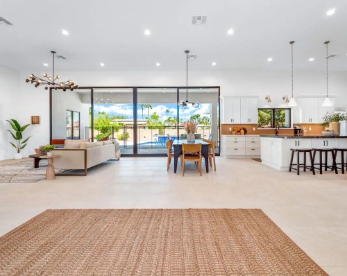 Modern open-concept living space with a dining area, kitchen, and large windows overlooking a pool. Bright and airy design.