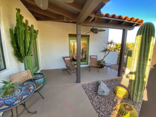 A cozy patio with a mosaic table, two chairs, cacti, and a view of the surrounding landscape.