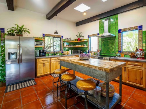 Bright kitchen with green tile accents, wooden cabinets, a large island, and stainless steel appliances.