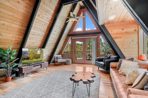 Cozy A-frame living room with wooden walls, large windows, a TV, and stylish furniture, overlooking a scenic view.