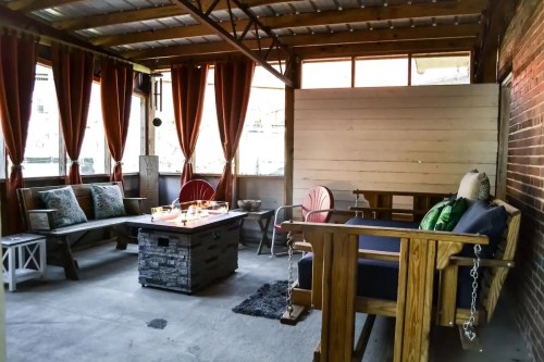 Cozy outdoor seating area with wooden furniture, a fire pit, and curtains, creating a warm and inviting atmosphere.