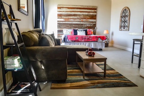 Cozy living space featuring a sofa, coffee table, and a bed with a rustic headboard in a bright room.