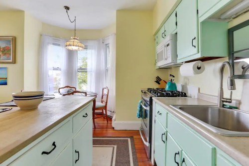 Bright kitchen with mint green cabinets, a sink, stove, and a cozy dining area with natural light.