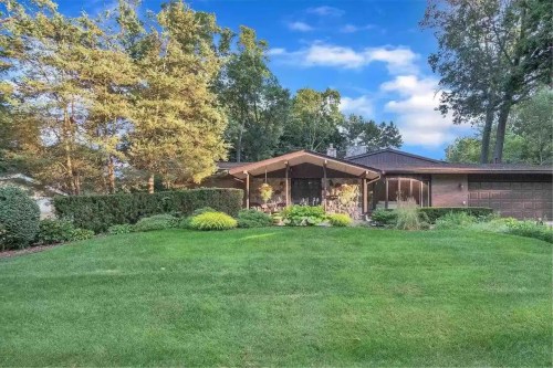A spacious lawn in front of a modern home surrounded by trees and shrubs under a blue sky.