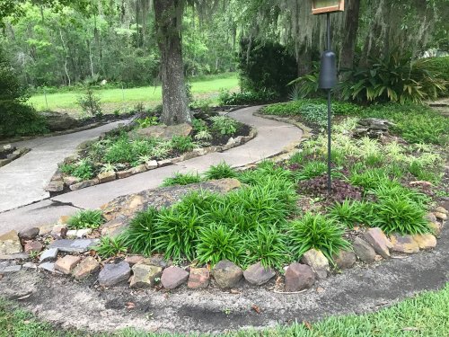 A winding garden path surrounded by lush greenery and stone borders, leading through a tranquil outdoor space.