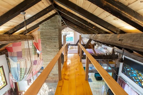 A cozy loft with wooden beams, a stone fireplace, and a walkway overlooking a living area with colorful quilts.