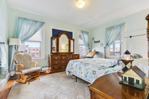 Bright bedroom with a bed, dresser, rocking chair, and large windows, featuring light blue walls and cozy decor.