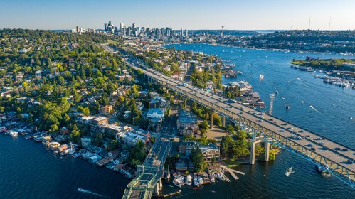 Aerial view of Seattle skyline and Lake Union with the Aurora Bridge spanning across water, houseboats, greenery, and city buildings in the background.