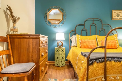 Cozy bedroom featuring a yellow bedspread, wooden furniture, a decorative mirror, and a stylish lamp.