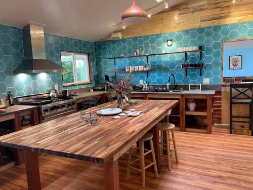 A modern kitchen with a wooden island, blue hexagonal tile walls, and stainless steel appliances. Bright and spacious design.