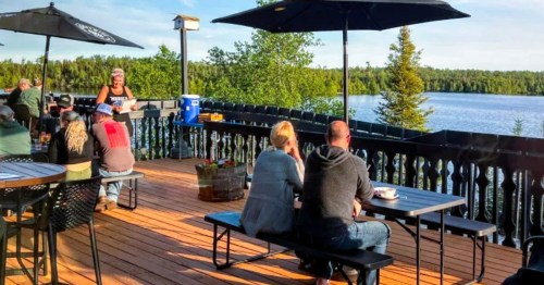 Views of a crowded patio at a Minnesota restaurant, overlooking a scenic lake surrounded by greenery.