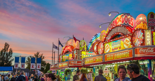 vendor and food booths aglow with neon lights under a sunset sky at the big e, a huge fall festival in springfield, massachusetts