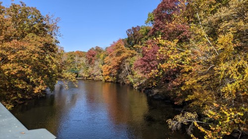 A serene river surrounded by vibrant autumn foliage under a clear blue sky.