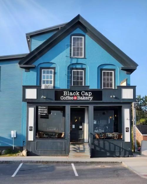 A blue building with a sign reading "Black Cap Coffee & Bakery," featuring outdoor seating and large windows.