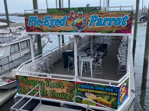 A boat named "Pie-Eyed Parrot" with outdoor seating, promoting happy hour and sunset cruises.