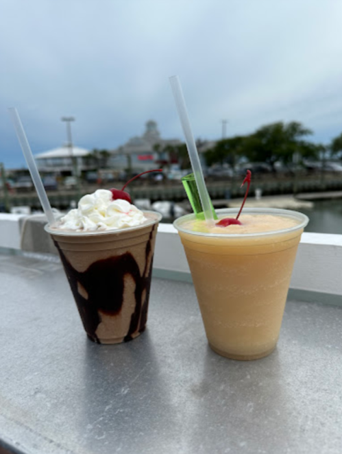 Two colorful drinks on a table: one with whipped cream and a cherry, the other a tropical smoothie with a green straw.