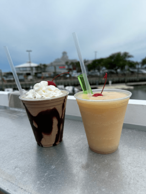 Two colorful drinks on a table: one with whipped cream and a cherry, the other a tropical smoothie with a green straw.