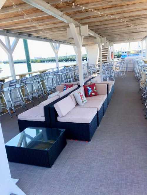 Outdoor seating area with cushioned sofas and a glass table, overlooking a waterfront view.