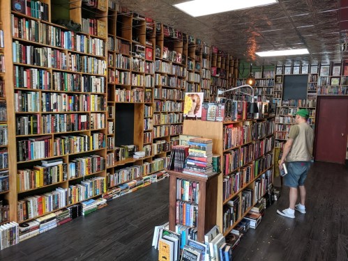 A cozy bookstore filled with tall shelves of books, featuring a person browsing near a central display.