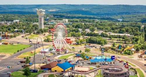 Aerial view of a vibrant amusement park featuring a large Ferris wheel and various attractions surrounded by greenery.