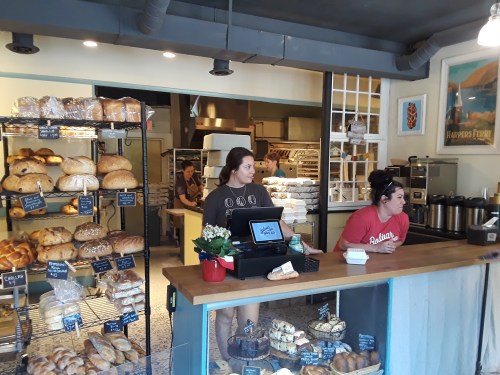 A cozy bakery with shelves of bread, two staff members at the counter, and a warm, inviting atmosphere.