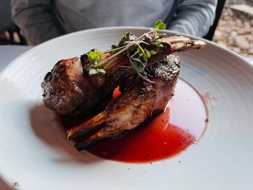 A plate featuring two grilled lamb chops garnished with microgreens, served in a red sauce.