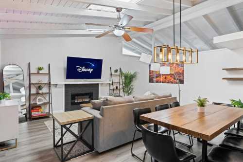 Modern living space featuring a cozy sofa, dining table, ceiling fan, and a TV displaying the Disney logo.