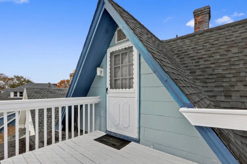 A blue and gray house with an A-frame roof, featuring a white door and a small balcony.