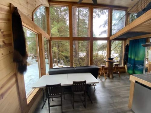 Cozy wooden interior with large windows, a dining table, and a view of trees outside.