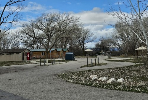 A quiet park area with cabins, a shelter, and a winding path under a cloudy sky, surrounded by bare trees.