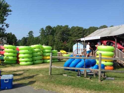 Colorful inflatable tubes stacked near a rental station, with people preparing for a water adventure in a sunny outdoor setting.