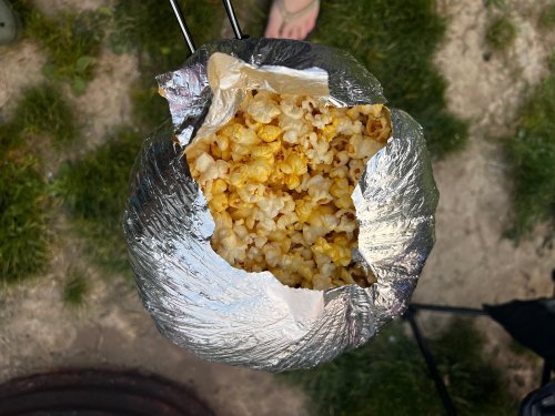A foil bag filled with freshly popped popcorn, resting on grass.